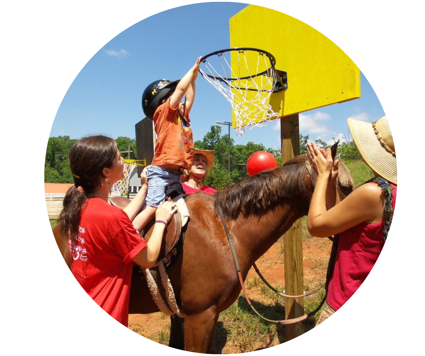 Child in orange shirt on a brown horse tossing a small red ball into a yellow basketball hoop. 