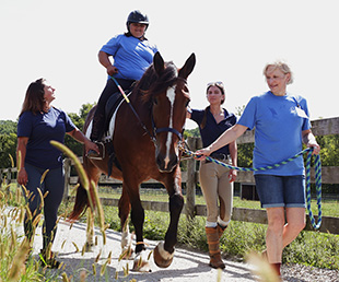 Client riding horse on outdoor trail with instructors